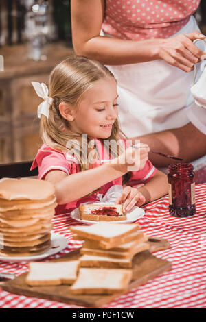 Cute smiling little girl manger de délicieux toasts avec de la confiture pour le petit déjeuner Banque D'Images