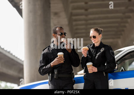 Les jeunes officiers de police avec du café et des beignes debout à côté de voiture sous le pont Banque D'Images