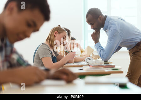 Vue latérale d'écoliers et d'écriture multiculturelle américaine africaine contrôle de l'enseignant Banque D'Images