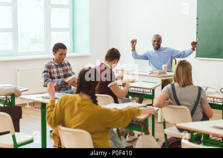 Groupe multiculturel de jeunes écoliers et smiling african american teacher with raising arms Banque D'Images