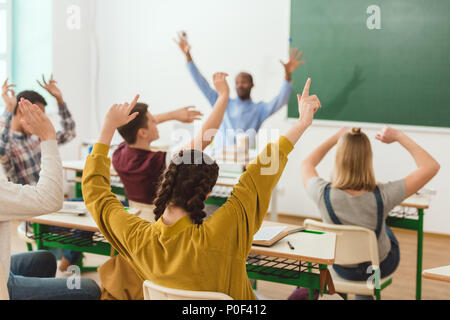 Vue arrière des écoliers et le repos d'enseignants raising arms Banque D'Images