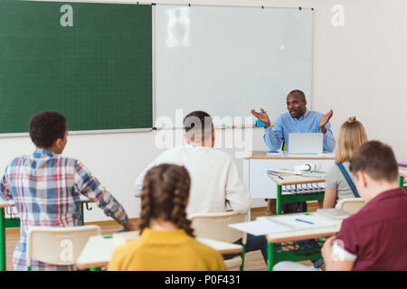 Vue arrière de l'école multiethnique étudiants adolescents afro-américains et avec des armes à l'échelle de l'enseignant Banque D'Images