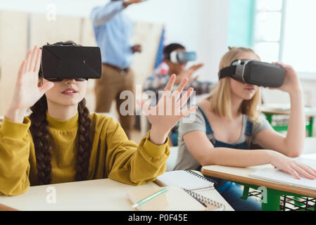 Deux jeunes écolières en utilisant les casques de réalité virtuelle et camarade de classe avec l'enseignant derrière Banque D'Images