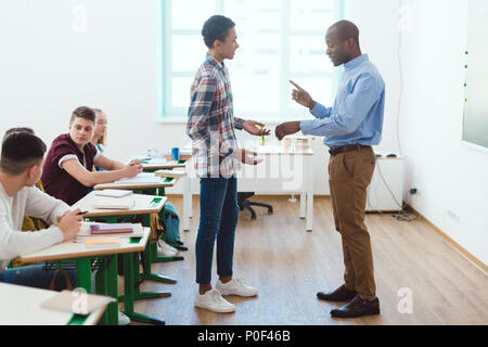 Vue latérale d'african american teacher pointing at montre-bracelet à retardataire en classe d'écolier Banque D'Images