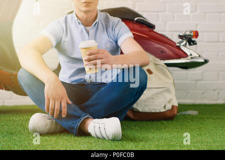 Cropped shot de jeune homme à la tasse de café à fo assis en face de scooter vintage Banque D'Images