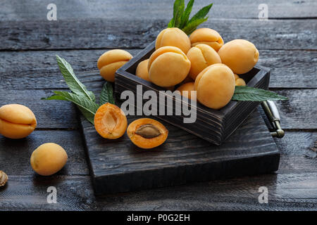 De délicieux abricots mûrs dans une boîte en bois sur fond sombre Banque D'Images
