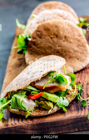 Des sandwichs pita farci au poulet, légumes et fromage sur planche à découper en bois. Banque D'Images