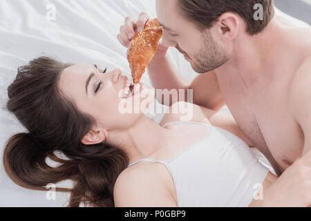Beau jeune homme se nourrir sa petite amie au lit avec croissant Banque D'Images