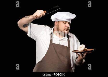 Chef holding couteau à viande et les beignes sur la plaque isolated on black Banque D'Images