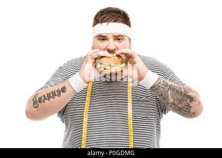 L'homme grassouillet avec ruban à mesurer et hamburger looking at camera isolated on white Banque D'Images