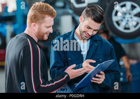 Automechanic jeunes montrant un client souriant presse-papiers à un atelier de réparation. Banque D'Images