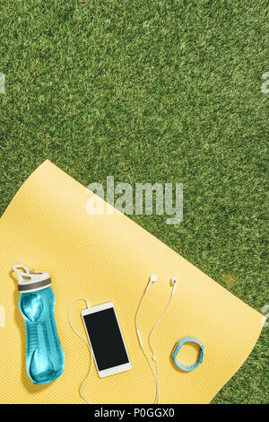 Mise à plat avec une bouteille d'eau, regarder, smartphone et écouteurs sur jaune mat sur pelouse verte Banque D'Images