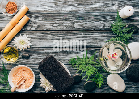 Vue de dessus de cailloux disposés, sel, d'huile, bâtons de bambou et orchidée, fleur dans un bol pour spa et massage sur fond de bois Banque D'Images