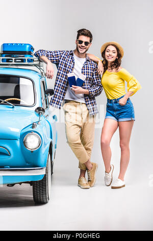 Beau jeune couple de voyageurs avec des billets debout à côté vintage car isolated on white Banque D'Images