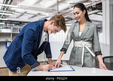 Beau jeune homme signature contrat alors que businesswoman pointing at il Banque D'Images