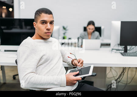 Handsome young businessman with tablet assis au bureau open space Banque D'Images