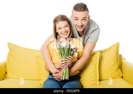 Portrait of smiling man hugging femme avec bouquet de tulipes jaunes sur canapé isolated on white Banque D'Images