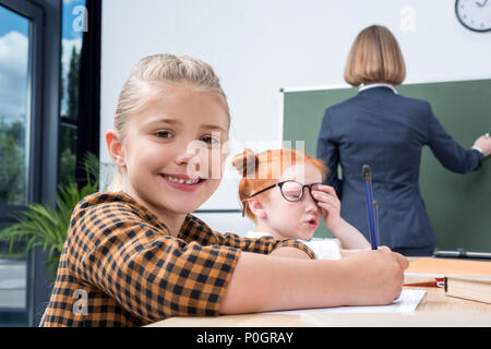 Vue arrière de l'enseignant écrit sur tableau noir alors que les étudiants qui étudient en classe Banque D'Images