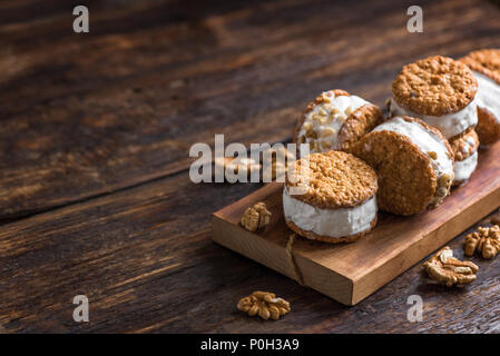 Sandwichs à la crème glacée avec les écrous et les cookies. Sandwichs à la crème glacée à la vanille sur fond de bois sombre. Banque D'Images