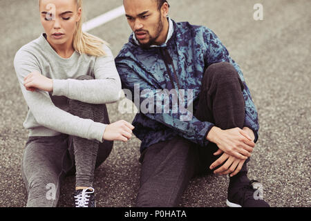 Fatigué à la young couple in sportswear assis sur un chemin ensemble reprendre leur souffle tandis que dehors pour une course Banque D'Images