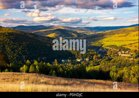 Belle campagne des Carpates au coucher du soleil. village en bas dans la vallée à l'ombre d'une montagne proche. beau ciel avec les nuages colorés. L'eau des Grands Banque D'Images