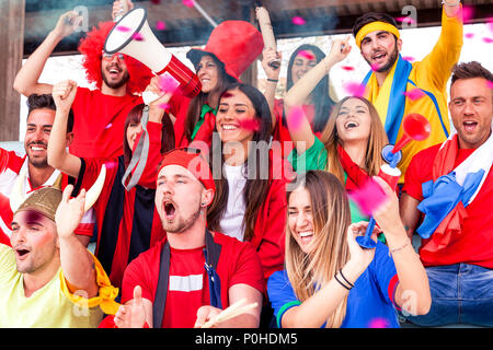 Groupe de fans vêtus de différentes couleurs en regardant un événement sportif dans les gradins d'un stade Banque D'Images