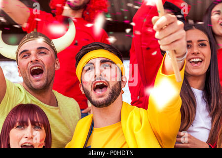 Groupe de fans vêtus de différentes couleurs en regardant un événement sportif dans les gradins d'un stade Banque D'Images