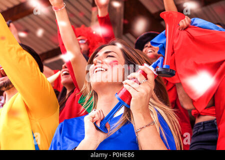 Groupe de fans vêtus de différentes couleurs en regardant un événement sportif dans les gradins d'un stade Banque D'Images