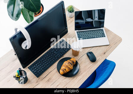 Portrait de casque sur l'écran d'ordinateur, ordinateur portable blanc avec écran vide, papeterie, croissant et café tasse sur la table Banque D'Images