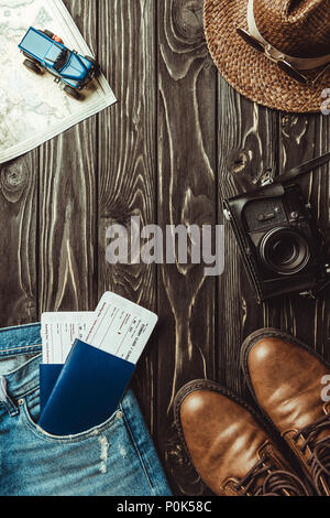 Mise à plat avec un pantalon en jean, chaussures, chapeau de paille, retro photo caméra, les passeports avec les billets sur la table en bois foncé Banque D'Images