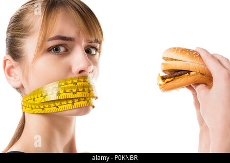 Jeune femme avec bouche attachés en ruban à mesurer en essayant de manger burger isolated on white Banque D'Images