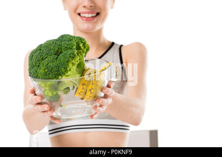 Cropped shot de slim femme avec brocoli couvert de ruban à mesurer dans un bol isolated on white Banque D'Images