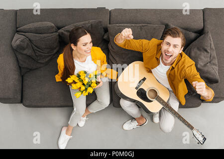 Vue supérieure de l'homme à la guitare et de poings en criant alors que sa petite amie holding bouquet sur la table à la maison Banque D'Images