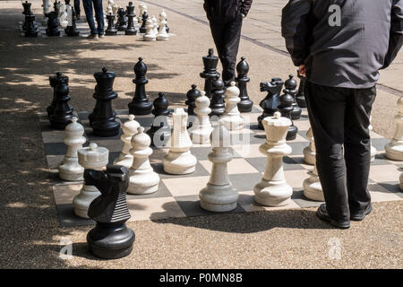 Deux personnes qui envisagent leur prochain déplacement tout en jouant aux échecs en plein air avec de grandes pièces, Victoria Gardens, Leeds, West Yorkshire, England, UK Banque D'Images