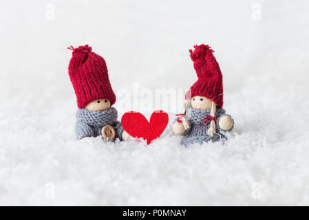 Couple poupées garçon et fille au chapeau tricoté chandails chauds et dans un décor de neige blanc moelleux, avec un cœur rouge entre eux. La métaphore de Banque D'Images