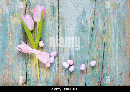 Composition de pâques avec deux fleurs de tulipe rose attaché avec du ruban de soie rose, fin peint les oeufs de Pâques sur le vieux fond en bois bleu, avec copie-espace, Banque D'Images