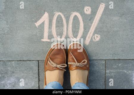Pieds femelles avec texte 100 % écrit sur le trottoir gris. Banque D'Images