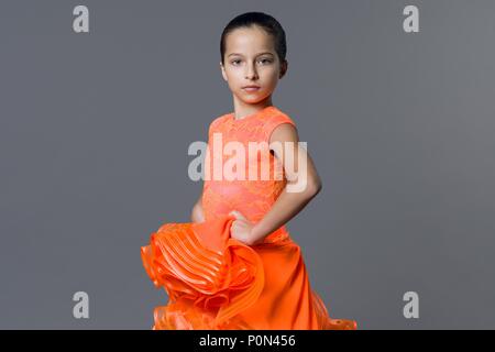 Portrait d'une petite fille 9-10 ans danseur. Sports danse de salon, latino. Jeune fille dans une robe orange sur un fond gris studio Banque D'Images