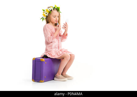 Vue latérale du kid sitting on suitcase violet et rouge à lèvres maquillage fait par isolated on white Banque D'Images