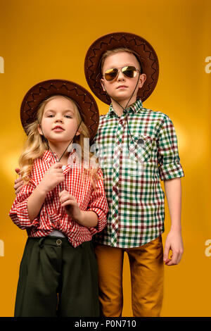 Élégant petit cowboy et cowgirl posant en chapeaux, isolé sur le jaune Banque D'Images