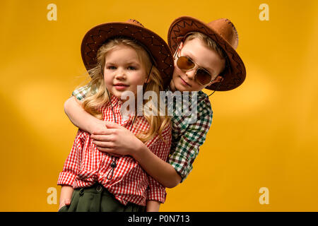 Élégant petit cowboy et cowgirl dans hats hugging isolé sur le jaune Banque D'Images