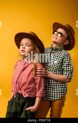 Élégant petit cowboy et cowgirl dans chapeaux, isolé sur le jaune Banque D'Images