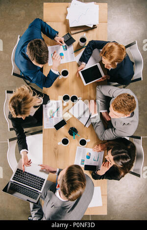 Vue aérienne de présentation aux partenaires dans le tableau avec les appareils numériques, des tasses à café et des documents Banque D'Images