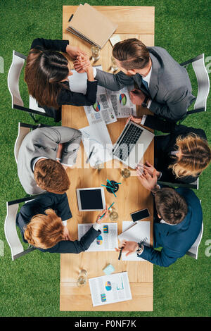 Vue de dessus de deux partenaires commerciaux faisant bras de fer alors que des collègues travaillant à table in office Banque D'Images