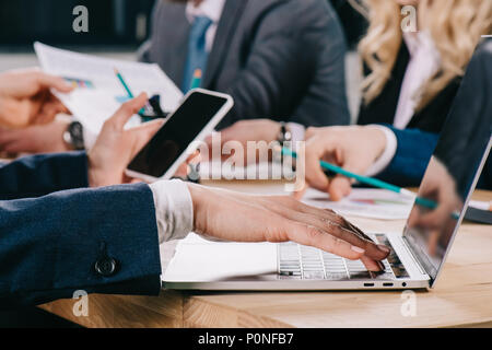 Portrait of businesswoman typing on laptop smartphone avec vos collègues tout en discutant à table in office Banque D'Images