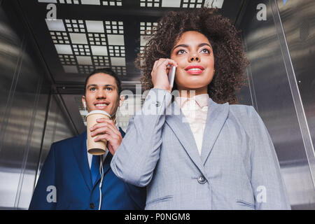 African American man in earphones with coffee cup debout dans ascenseur avec Woman talking on phone Banque D'Images