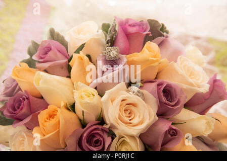 Belle photo aux couleurs avec les anneaux de mariage de diamant située au-dessus d'un bouquet de roses colorées Banque D'Images