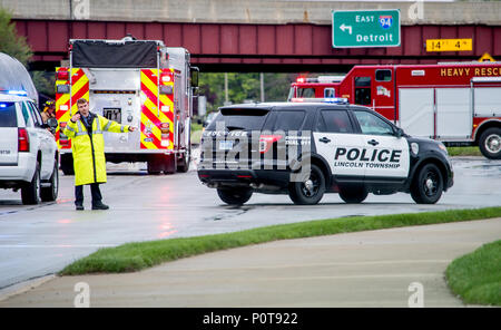 18 mai 2018 MI Stevensville USA ; un homme de la police dans des vêtements de pluie dirige le trafic à la scène d'un accident grave, avec des camions de pompiers en attente derrière lui Banque D'Images