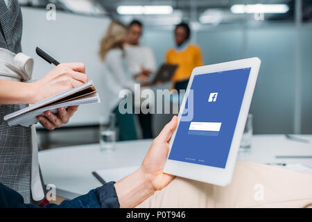 Businessman holding tablet avec facebook sur écran au bureau moderne tout en collègue prendre des notes Banque D'Images