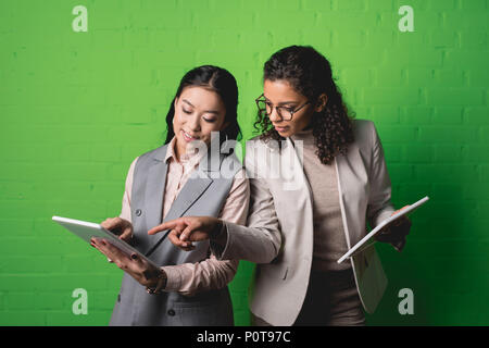 Femmes d'Afrique et d'Asie travailler avec tablettes numériques en face de mur vert Banque D'Images